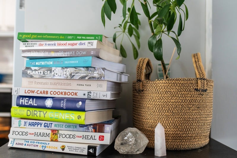 Stack of natural health and nutrition books next to a potted plant.